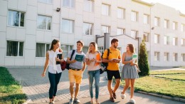 Five friendly students are walking after they passed test outside the college building and discuss the project